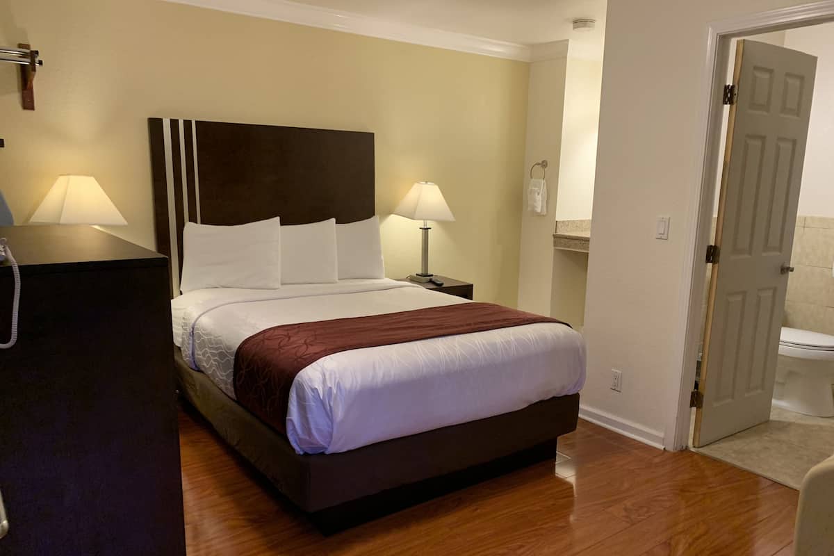 A hotel room with a large bed, two bedside lamps, a wooden floor, and a door leading to a bathroom.