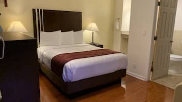 Habitación de hotel con una cama grande, dos lámparas de noche, piso de madera y una puerta que da a un baño.