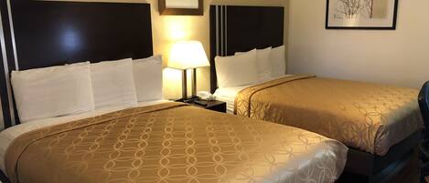 A hotel room with two beds, a nightstand with a lamp, and framed artwork on the walls.