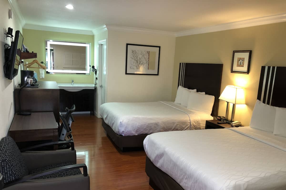 A hotel room with two beds, a desk with a chair, a small kitchenette, and a bathroom.