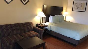 A hotel room with a striped sofa, a single bed with a quilt, a nightstand with a lamp, and a wooden floor.