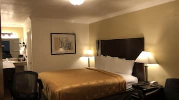 A hotel room with a bed, two bedside lamps, a desk with a chair, a framed picture on the wall, and a ceiling light.