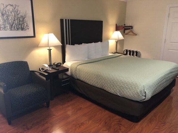 A hotel room with a bed, two bedside lamps, a chair, a desk with a telephone, and a framed picture on the wall.