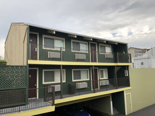 Un edificio residencial de dos plantas con balcones, un garaje y una cerca verde.
