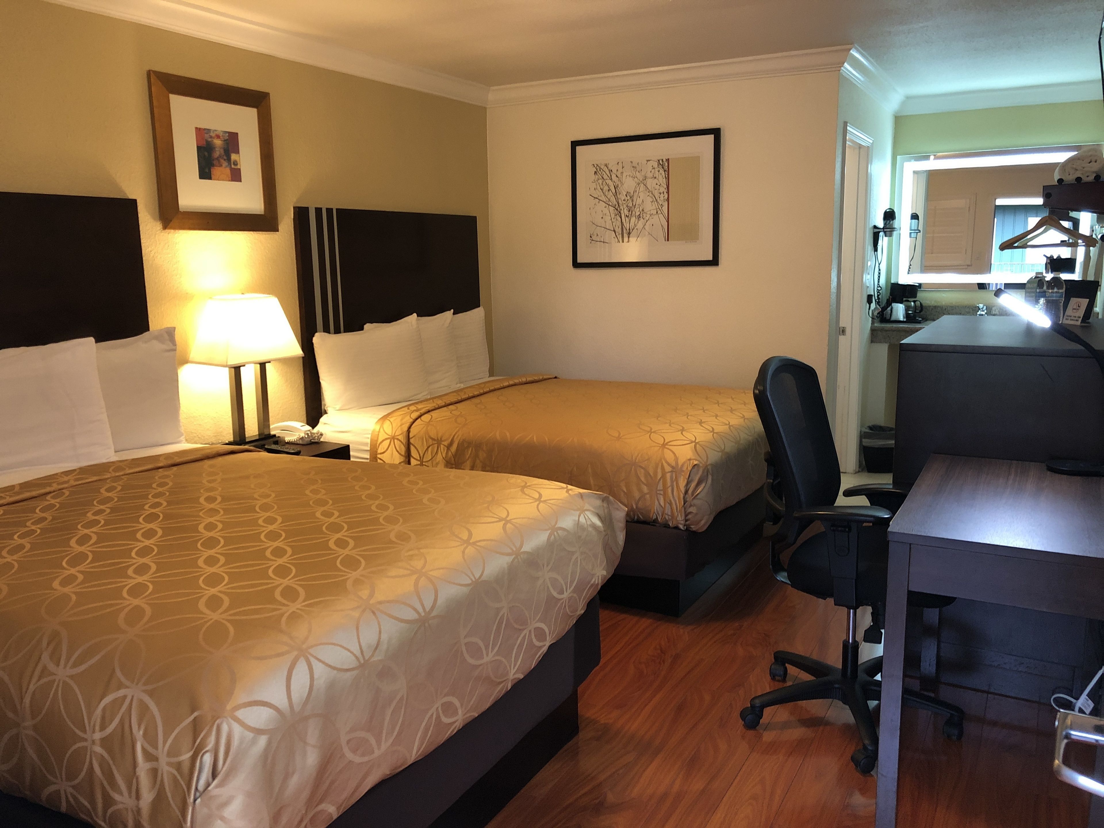 A hotel room with two beds, a desk, and a chair. There are framed pictures on the walls.