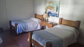 Una habitación con dos camas de madera, un escritorio con una lámpara y un cuadro en la pared.