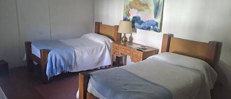 Una habitación con dos camas de madera, un escritorio con una lámpara y un cuadro en la pared.