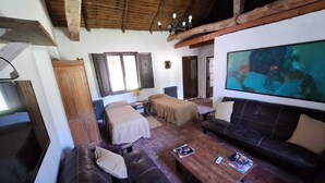 Ein gemütliches Zimmer mit Holzbalkendecke, einem großen Fernsehbildschirm, zwei Betten, einer Couch und einem Couchtisch.