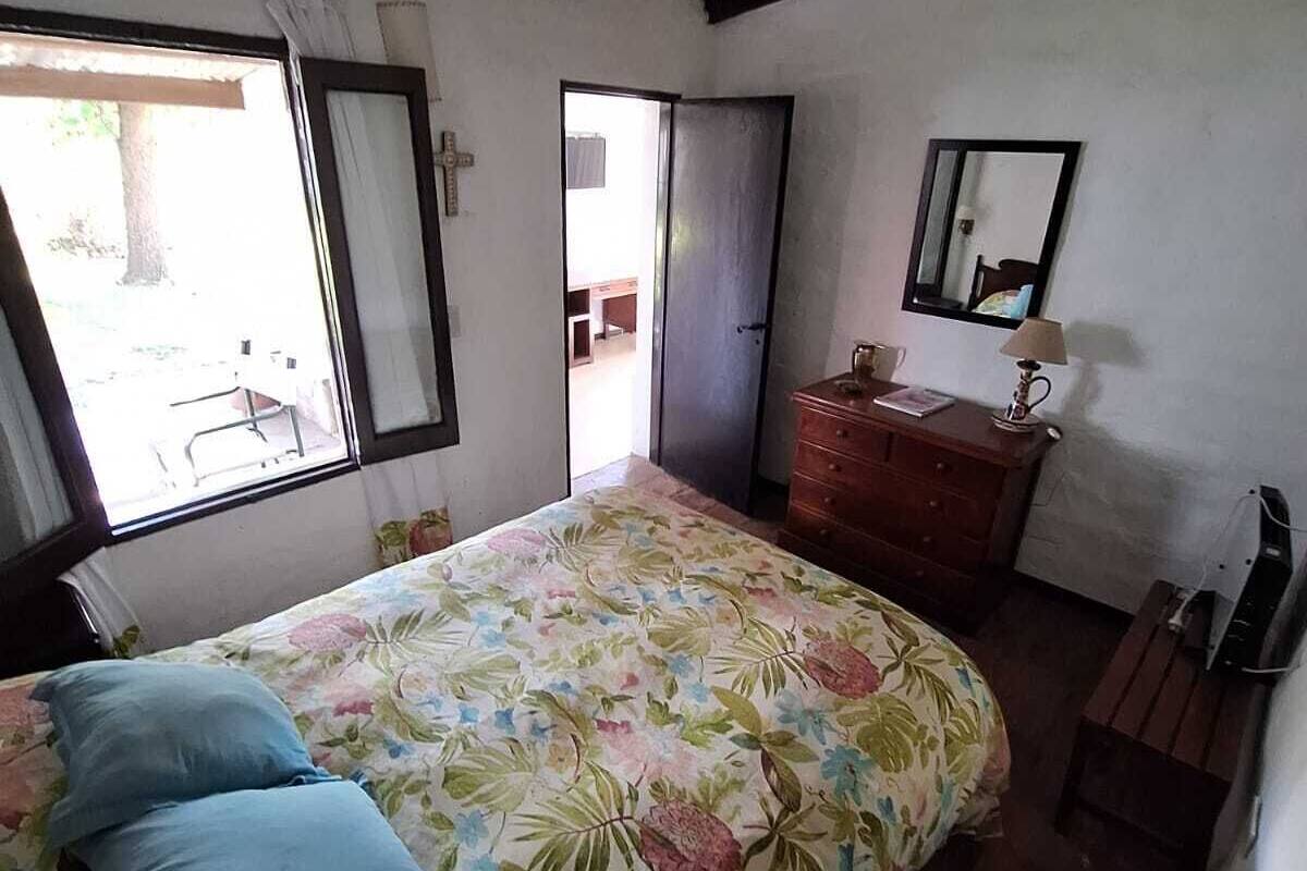 Un dormitorio con cubrecama floral, cómoda de madera, espejo y ventana con vistas al exterior.