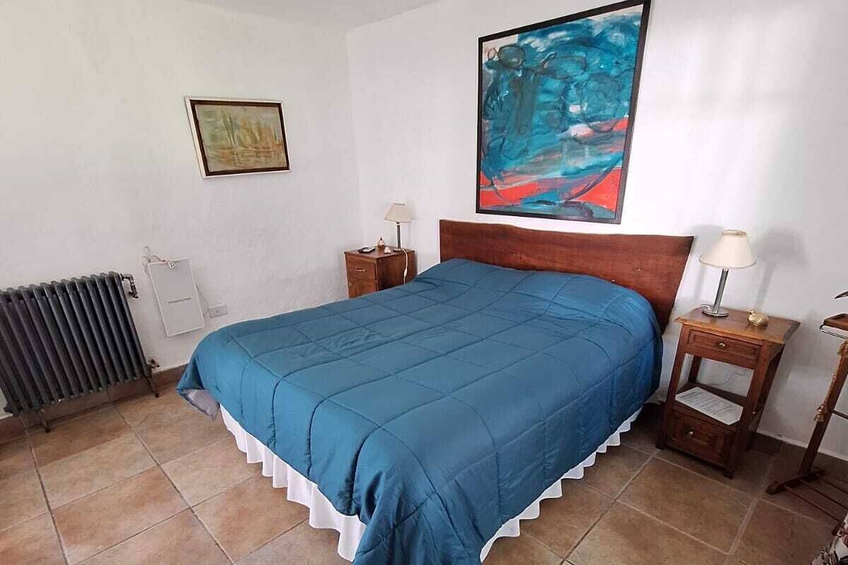 Un dormitorio con una cama, dos mesitas de noche, un radiador y un cuadro en la pared.