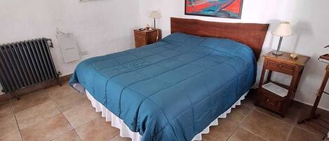 Un dormitorio con una cama, dos mesitas de noche, un radiador y un cuadro en la pared.
