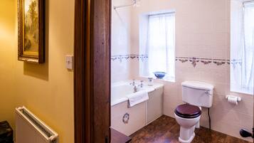 A bathroom with a wooden floor, a white toilet, a bathtub, and a window.
