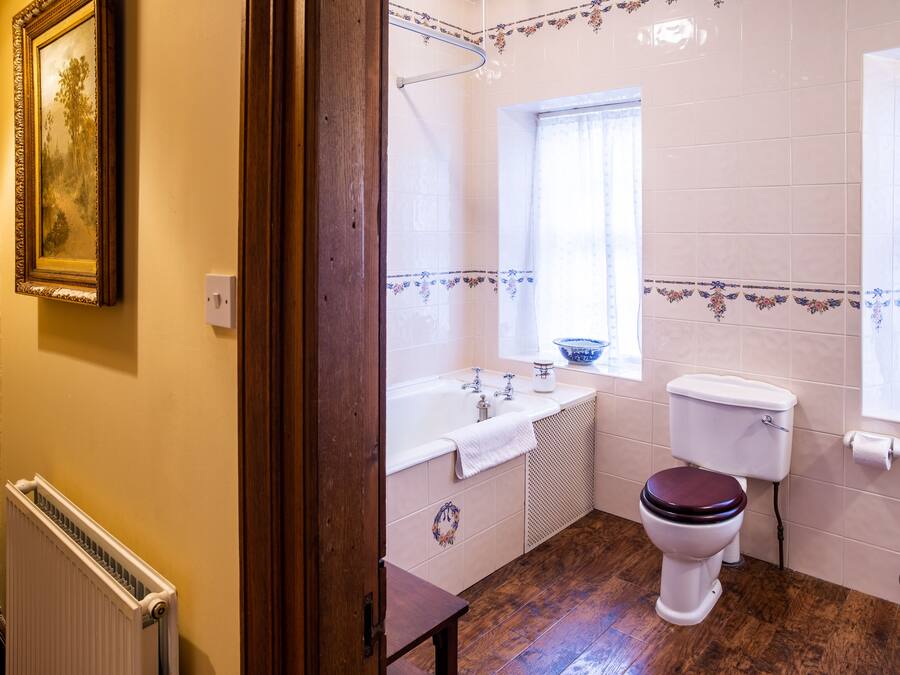 A bathroom with a wooden floor, a white toilet, a bathtub, and a window.