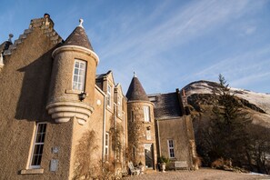 A historic stone building with multiple towers and a large rock formation in the background.