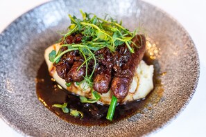 A dish with sausages, greens, and mashed potatoes on a textured plate.
