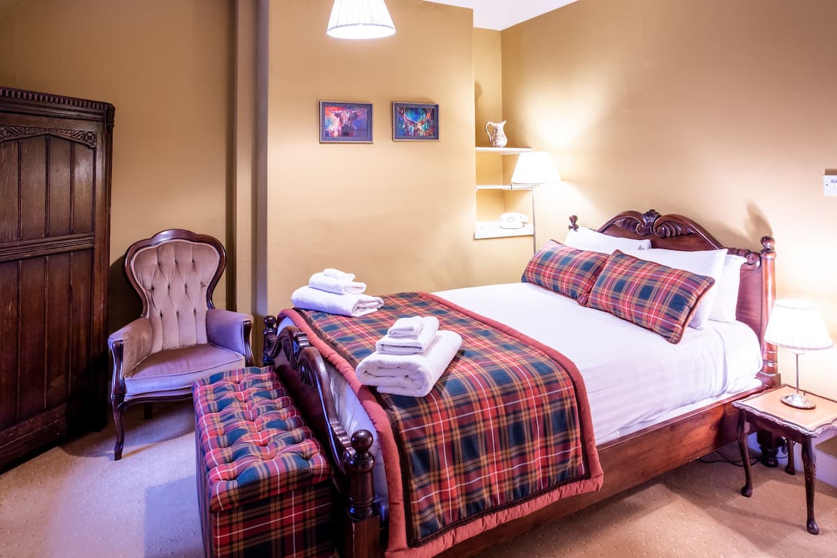 Une chambre à coucher bien aménagée, avec un grand lit, une chaise, une table de chevet et deux lampes fixées au mur.