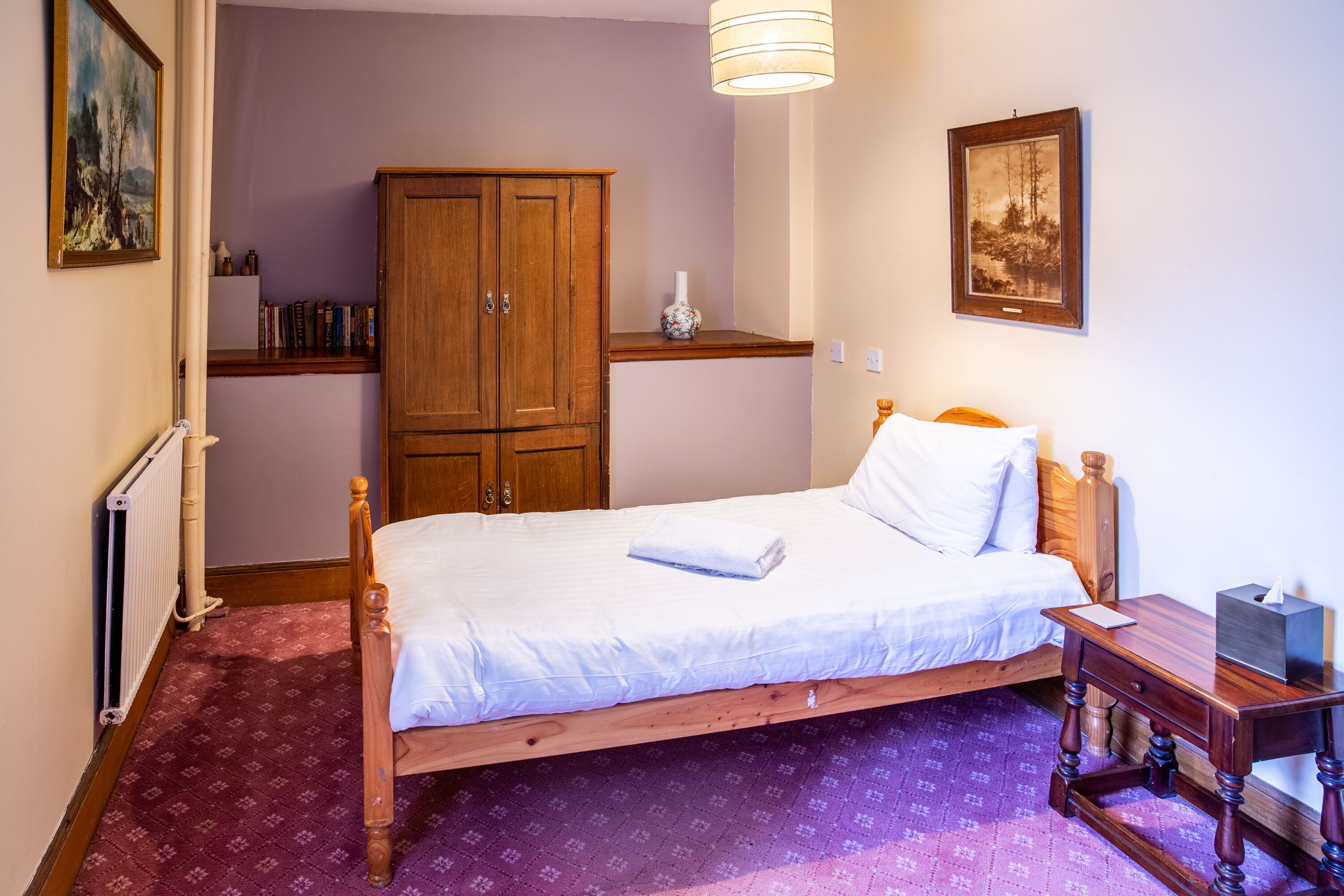 Quarto com cama de madeira, mesa de cabeceira, guarda-roupa e radiador.