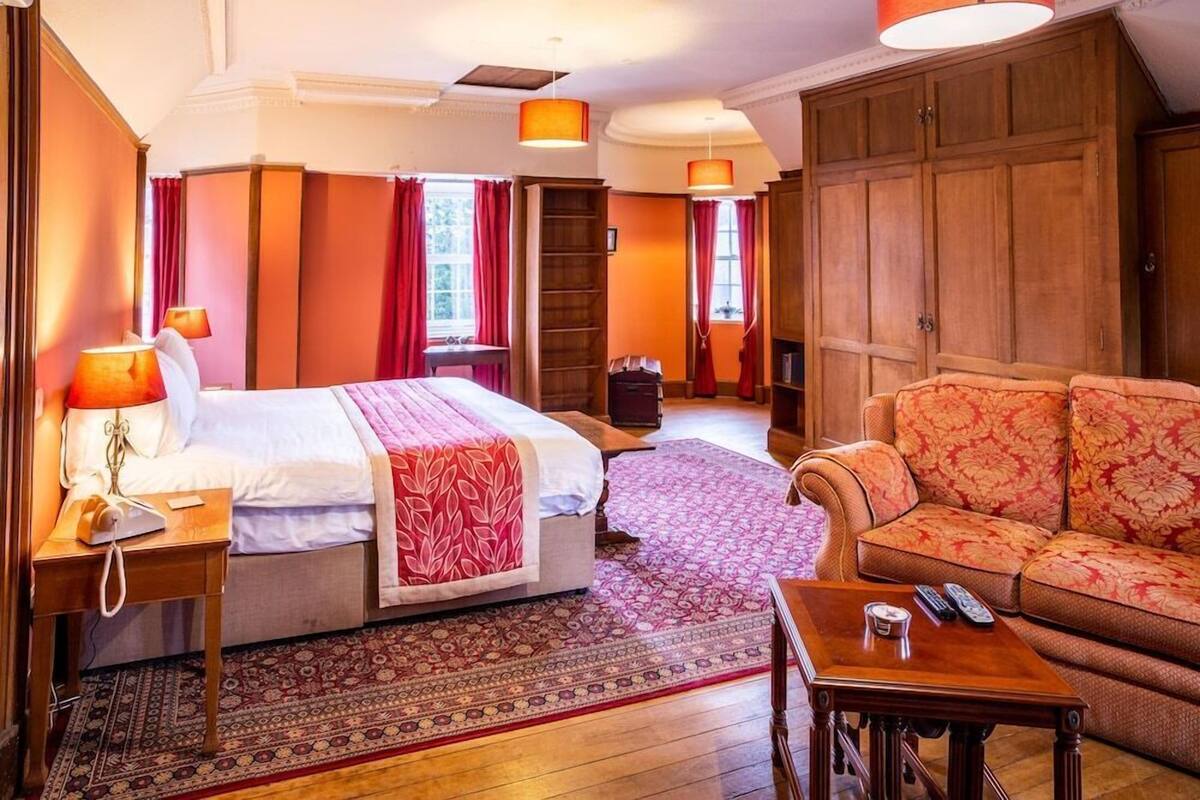 Une chambre d’hôtel avec un lit, un canapé, une armoire en bois, une table de chevet et un tapis à motifs.