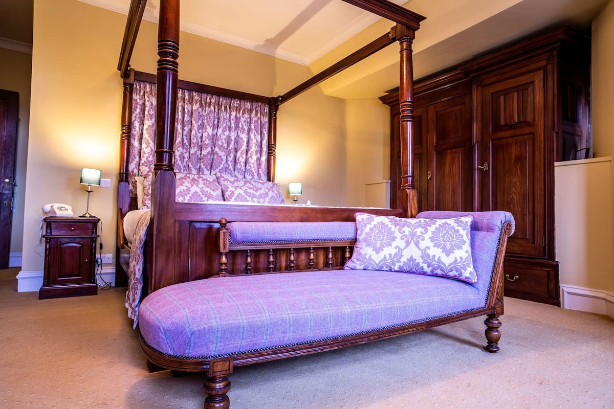 Un lit à baldaquin avec un banc assorti, une table de chevet avec une lampe et une grande armoire en bois.