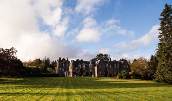 A large, historic building with multiple towers and a well-maintained lawn in front.