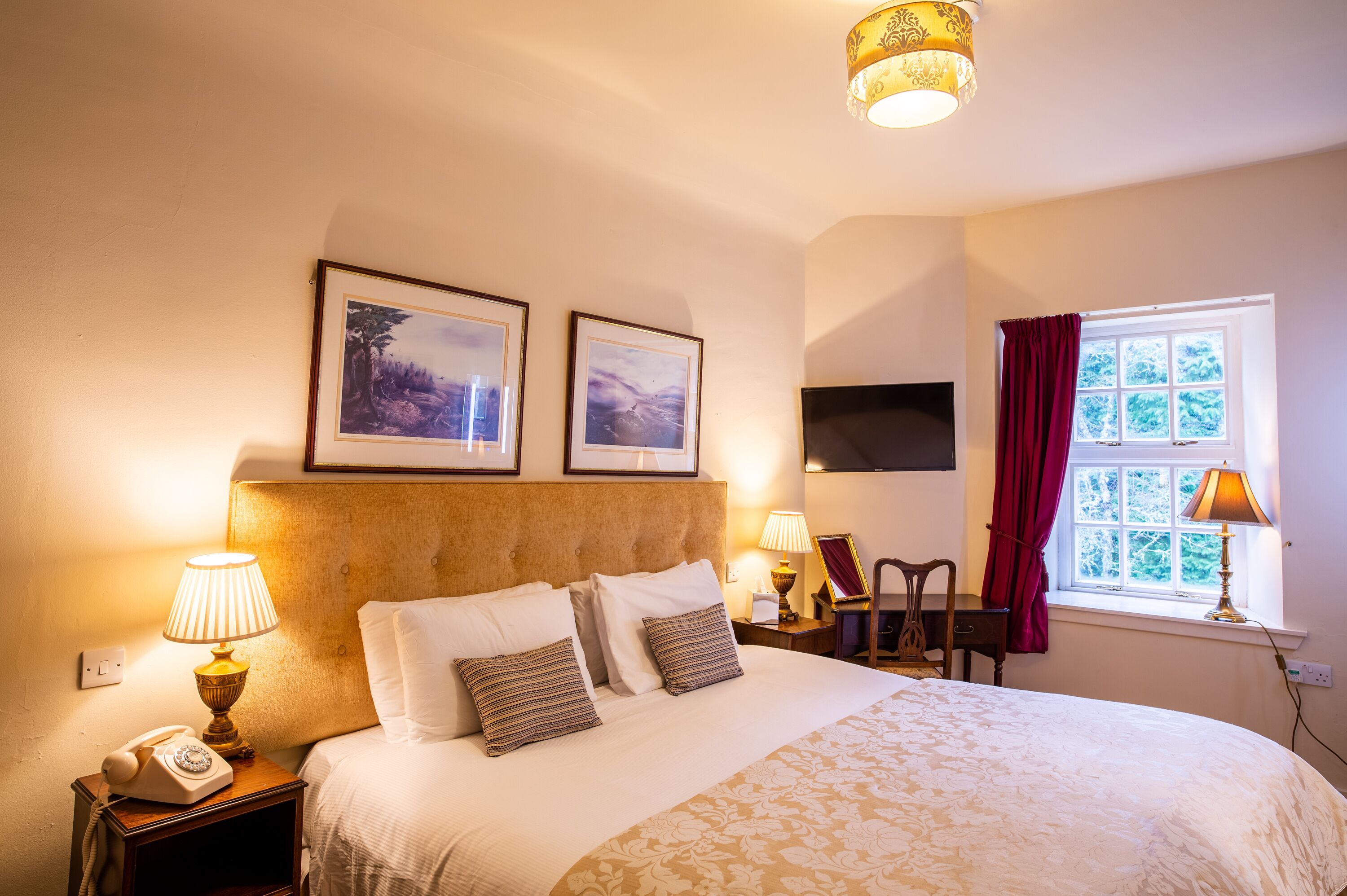 Une chambre d’hôtel avec un grand lit, deux tableaux encadrés au mur, une télévision, un bureau avec une chaise et une fenêtre avec des rideaux.