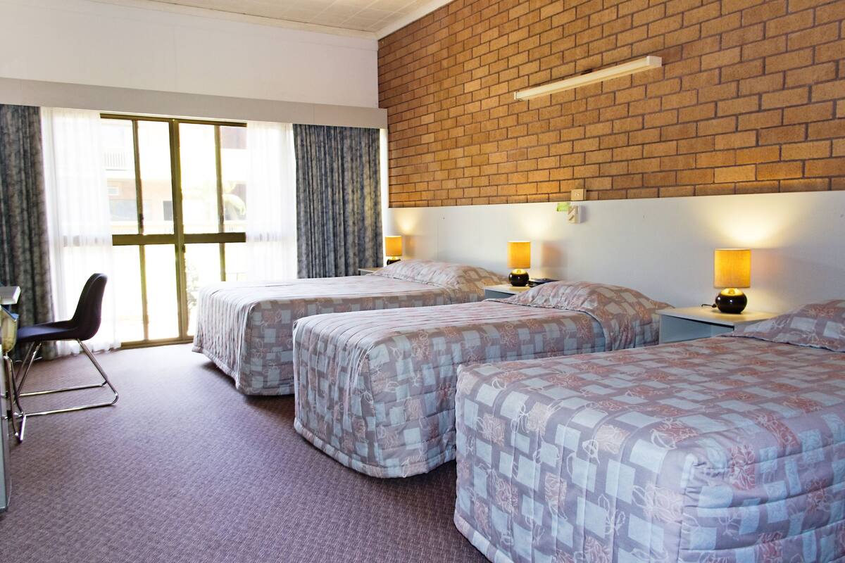 A hotel room with two beds, a desk, and a chair. There are two bedside lamps and a window with curtains.