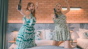 Two people holding champagne bottles on a bed with a brick wall background. - Litchfield Outback Resort (Batchelor)
