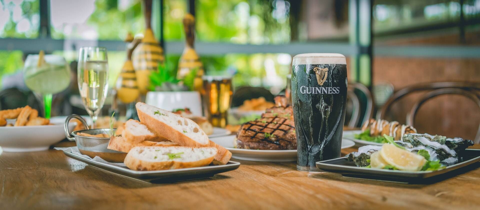 A dining table with various dishes, including bread, a steak, and seafood, along with a glass of Guinness beer.