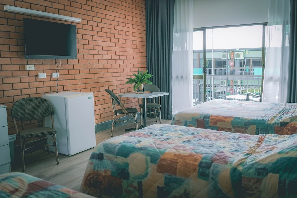A hotel room with two beds, a small table with a chair, a TV mounted on the wall, and a balcony with a view.