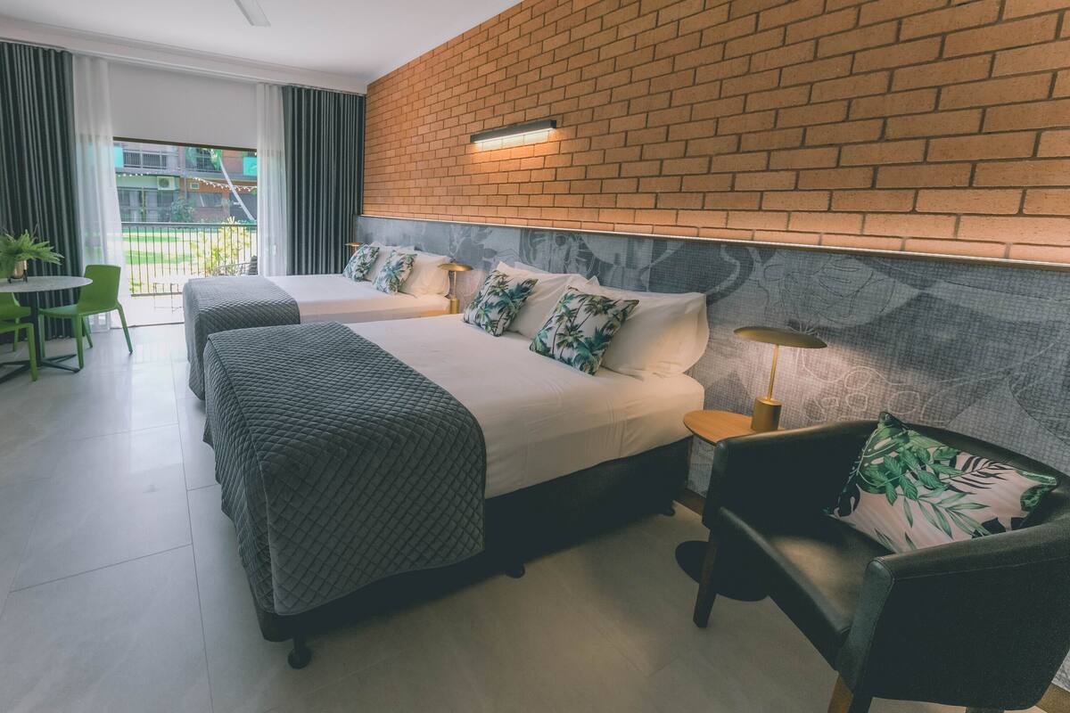 A hotel room with two beds, a balcony, a green chair, and a small table.