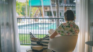 A woman sitting by a window with a view of a pool and buildings. - Litchfield Outback Resort (Batchelor)