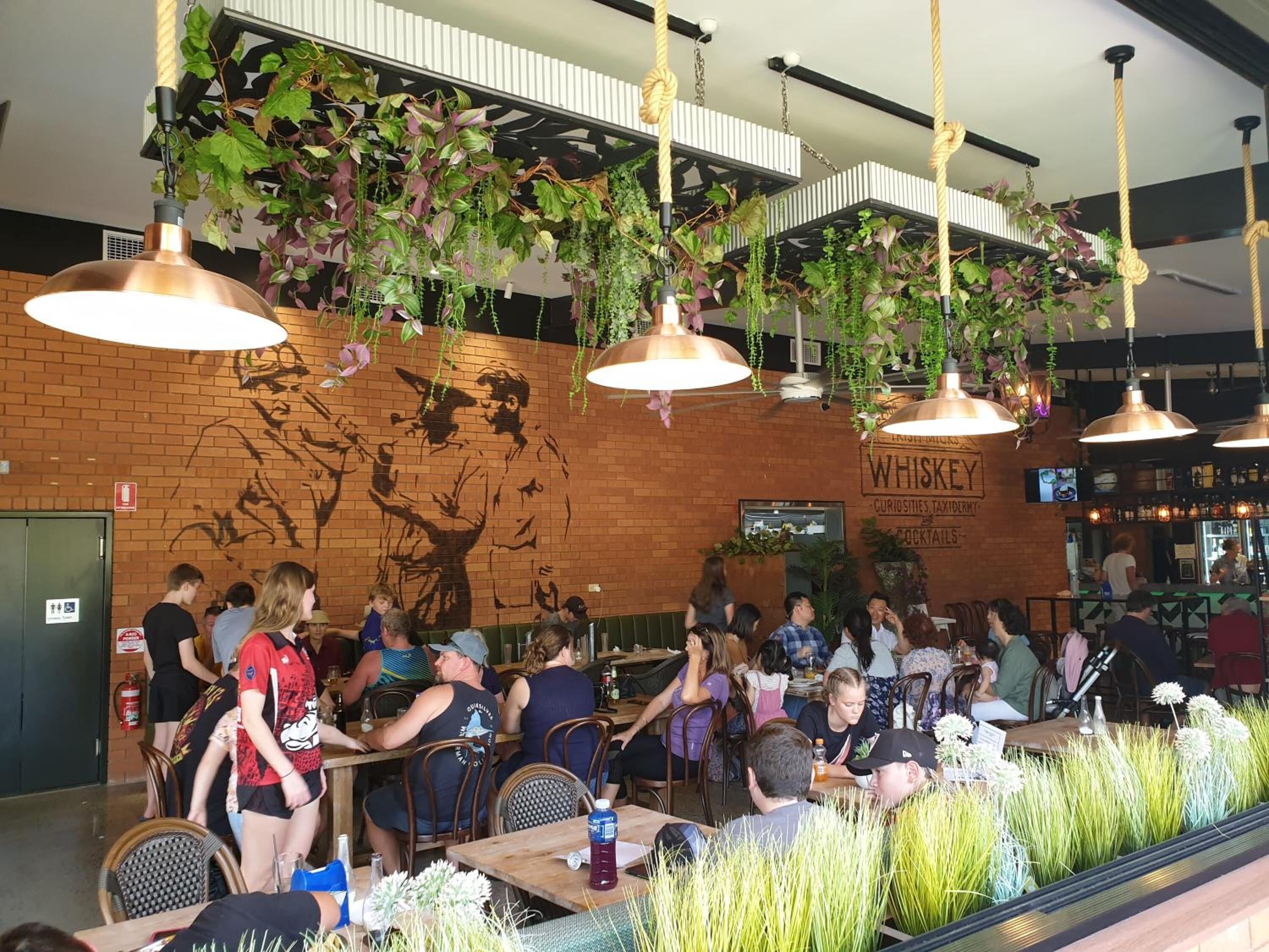 A restaurant with hanging plants, a brick wall mural, and a whiskey sign.