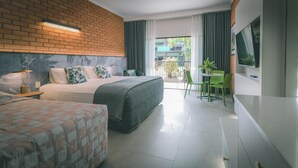 A hotel room with a brick wall, a bed with a quilted cover, a second bed, a green chair, a small table, and a TV on the wall. - Litchfield Outback Resort (Batchelor)