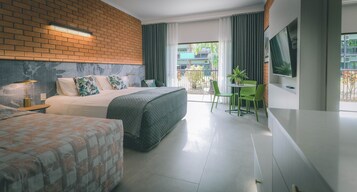 Una habitación de hotel con pared de ladrillo, una cama con cubierta acolchada, otra cama, una silla verde, una mesita pequeña y un televisor en la pared.