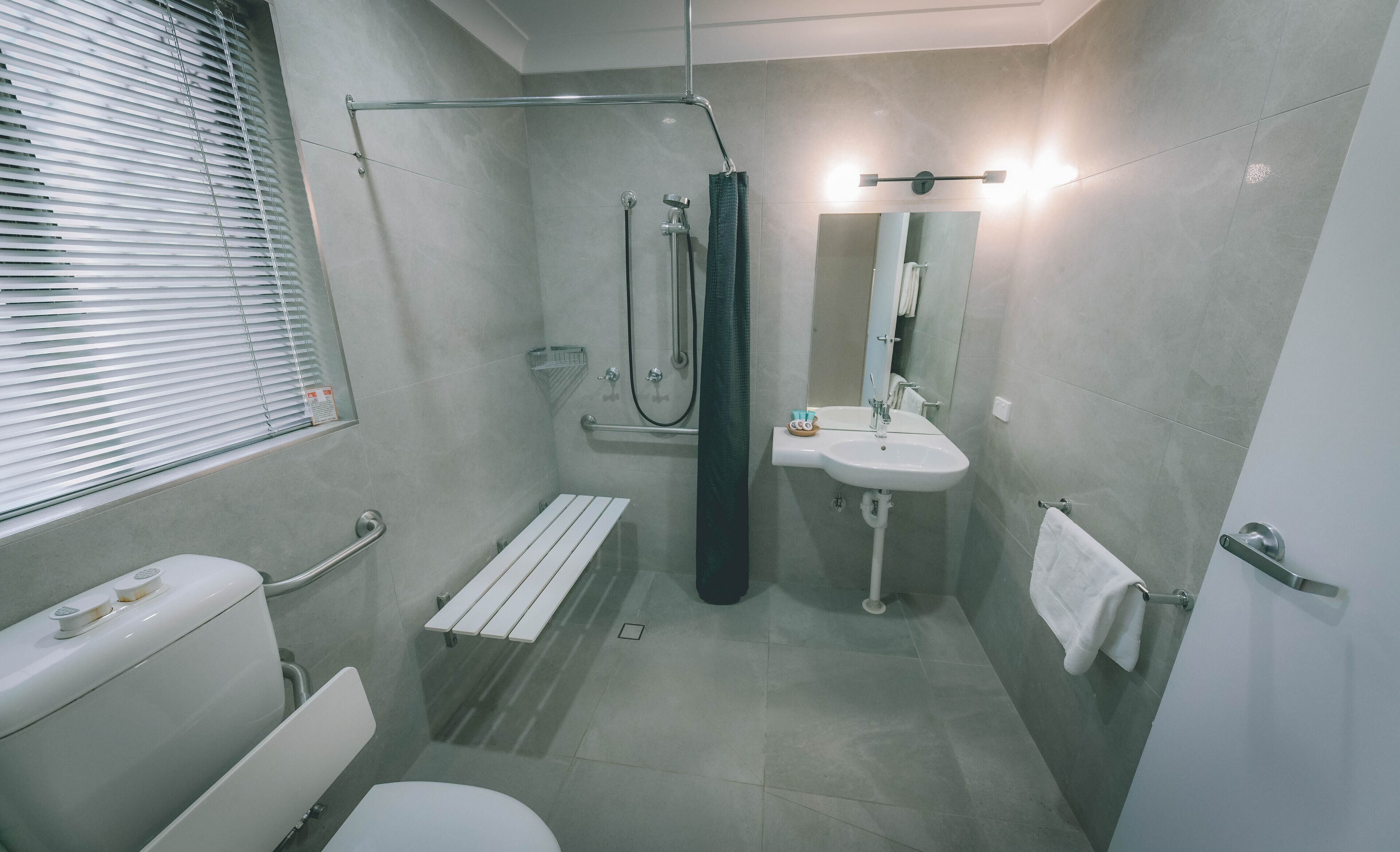 Un baño moderno con inodoro, ducha, lavamanos y un perchero para toallas.