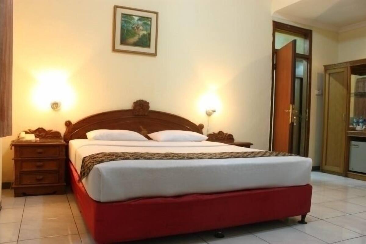 A single bed with a wooden headboard, two bedside lamps, a nightstand, and a painting on the wall.