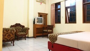 Quarto de hotel com cama, duas poltronas, escrivaninha e televisão, além de amplas janelas.