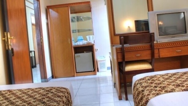 Quarto de hotel com cama, escrivaninha com televisão, guarda-roupa e pequeno frigorífico.