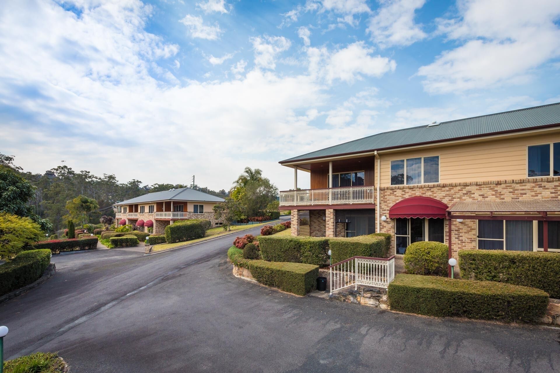A two-story hotel with a balcony, a covered entrance, and a well-maintained garden.