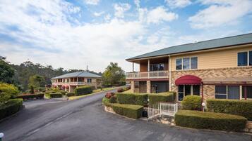 A two-story hotel with a balcony, a covered entrance, and a well-maintained garden.