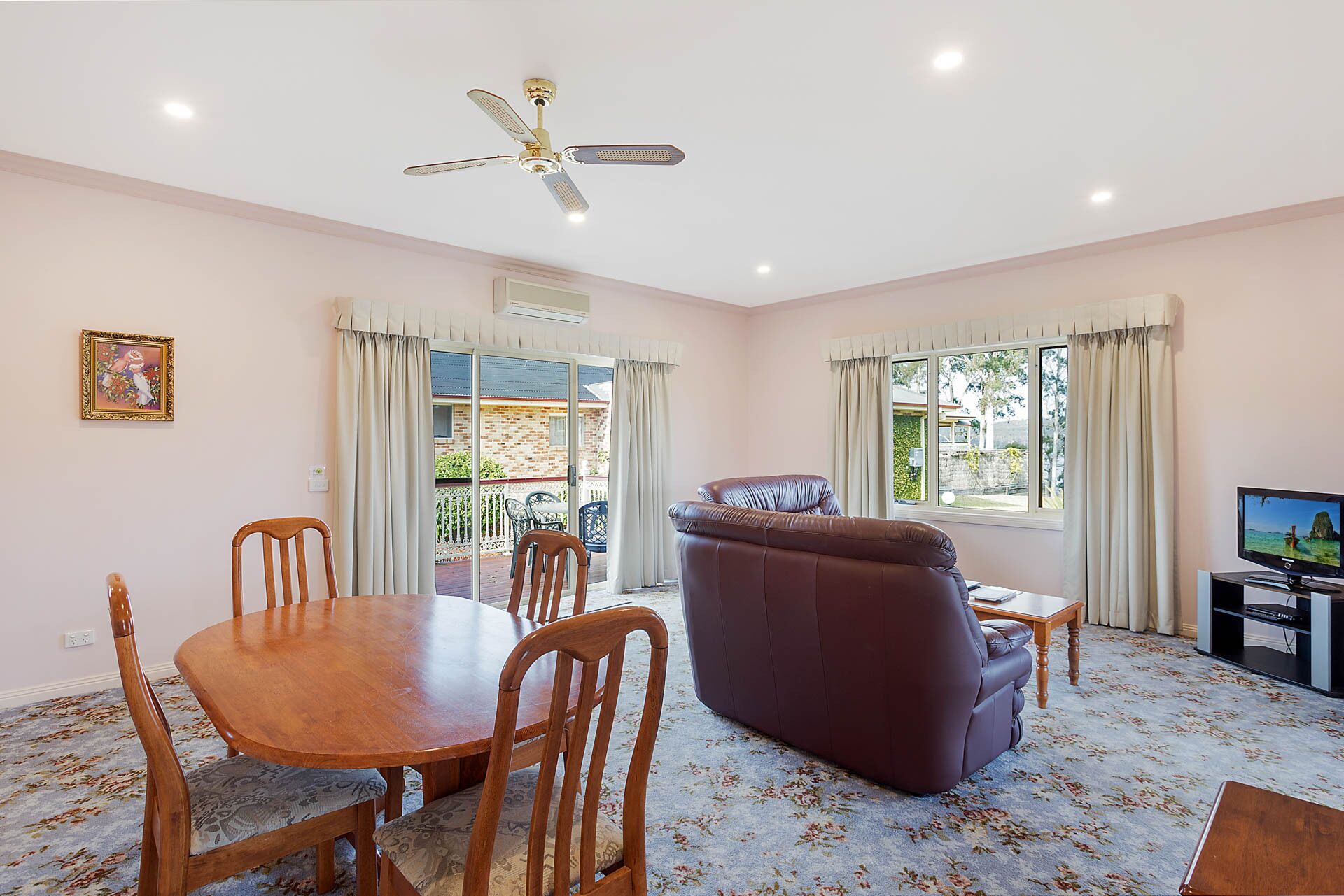 A spacious living room with a dining area, a leather sofa, a ceiling fan, and a television.