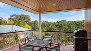 An outdoor patio with a table and chairs, a grill, and a view of trees and a building in the background.