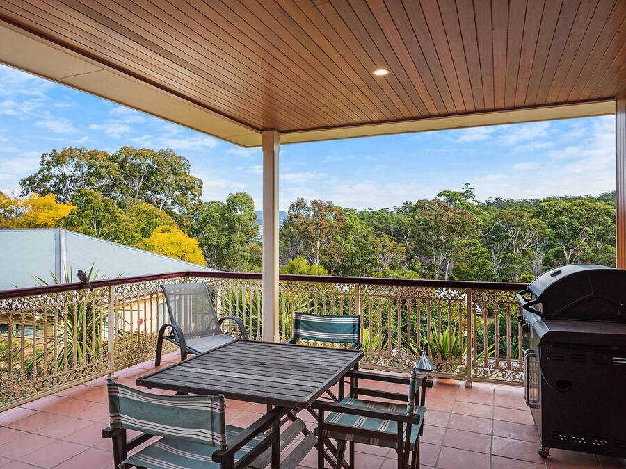 An outdoor patio with a table and chairs, a grill, and a view of trees and a building in the background.