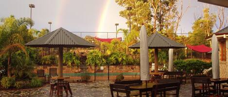 An outdoor patio with stone flooring, wooden tables and chairs, and covered seating areas.