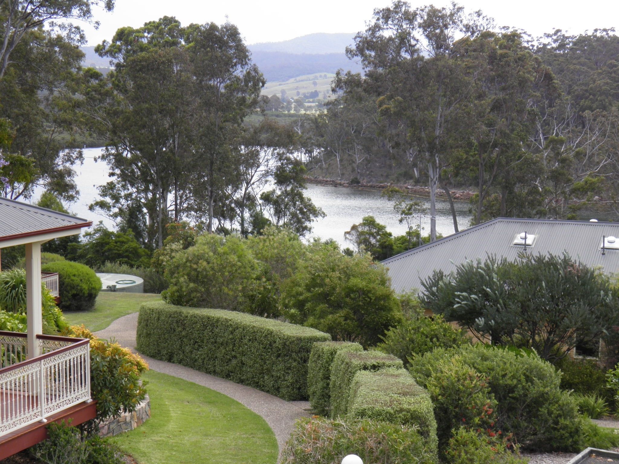A residential property with a landscaped garden, a curved pathway, and a view of a lake and hills in the background.