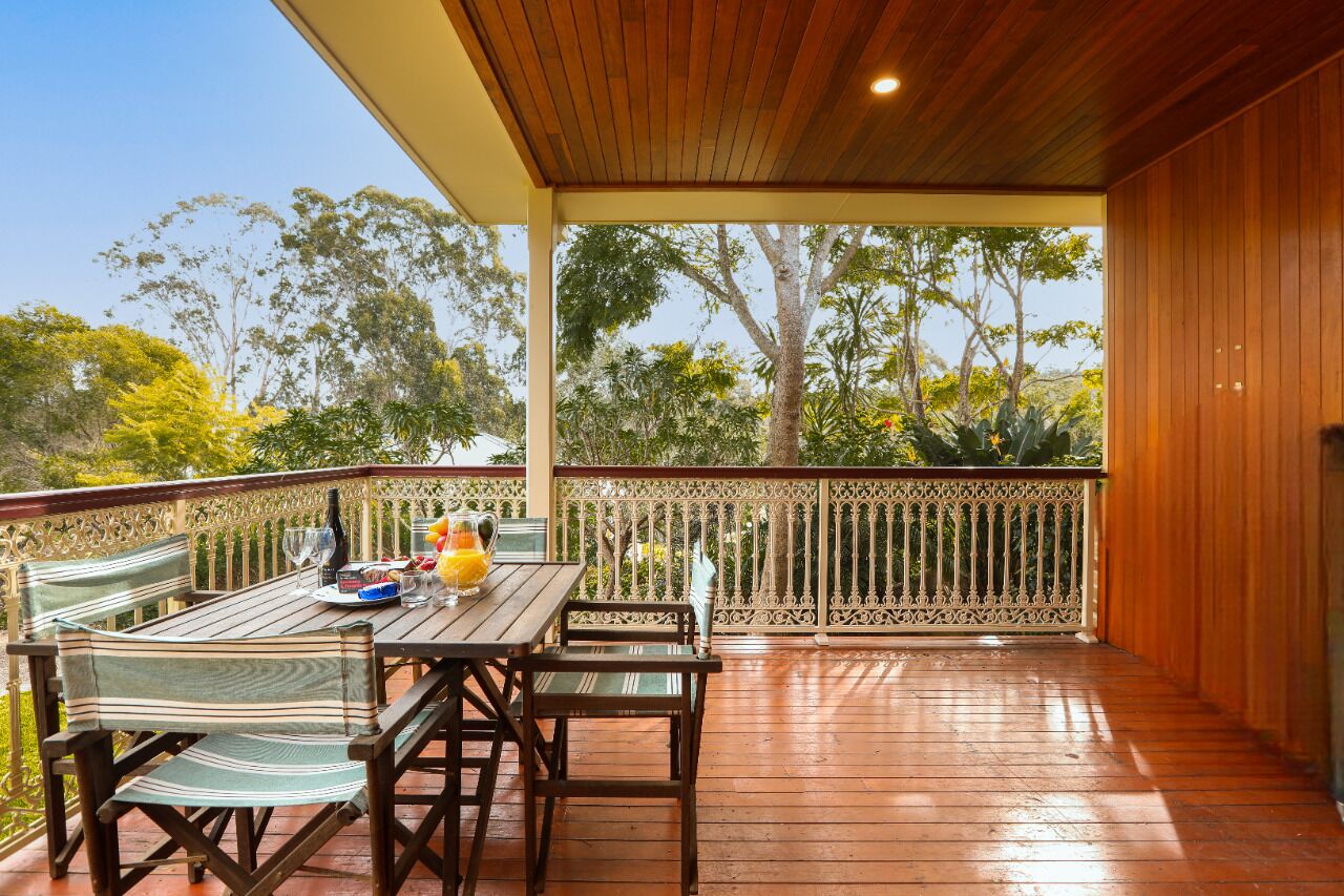 A wooden deck with a table and chairs, surrounded by a railing with a view of trees.