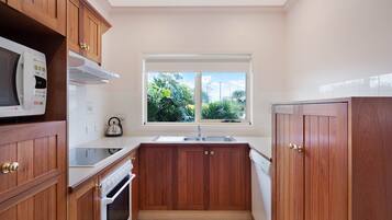 A compact kitchen with wooden cabinets, a microwave, an oven, a sink, and a window with a view of greenery.