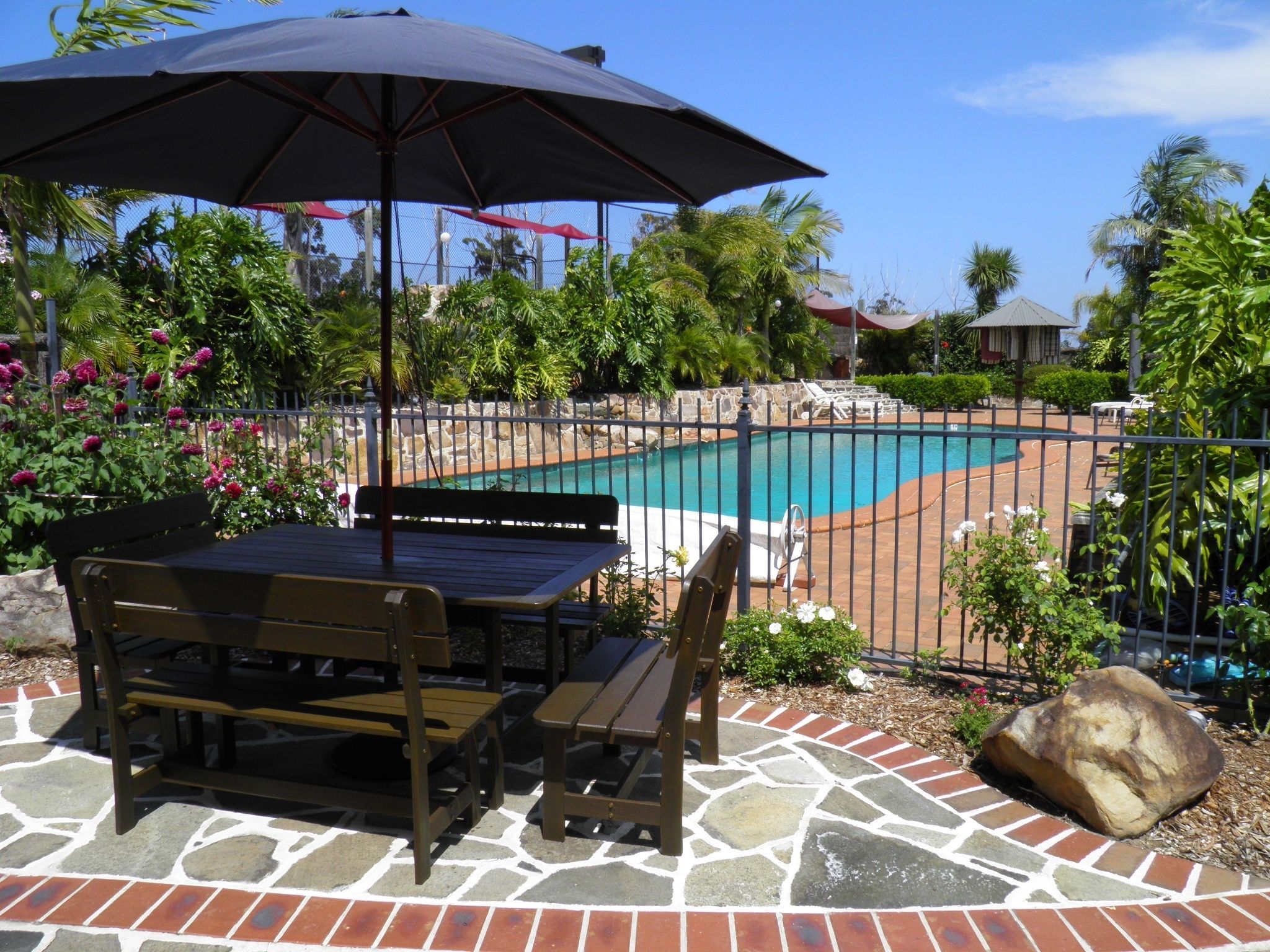 A pool area with a stone patio, a wooden table and bench, and an umbrella.
