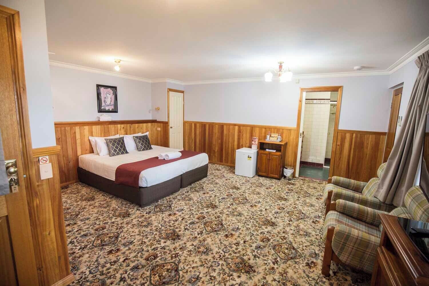 A hotel room with a bed, a small desk, a chair, and a carpeted floor.