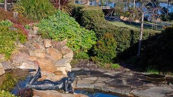 Un jardín ajardinado con un estanque, rocas y una casa al fondo.